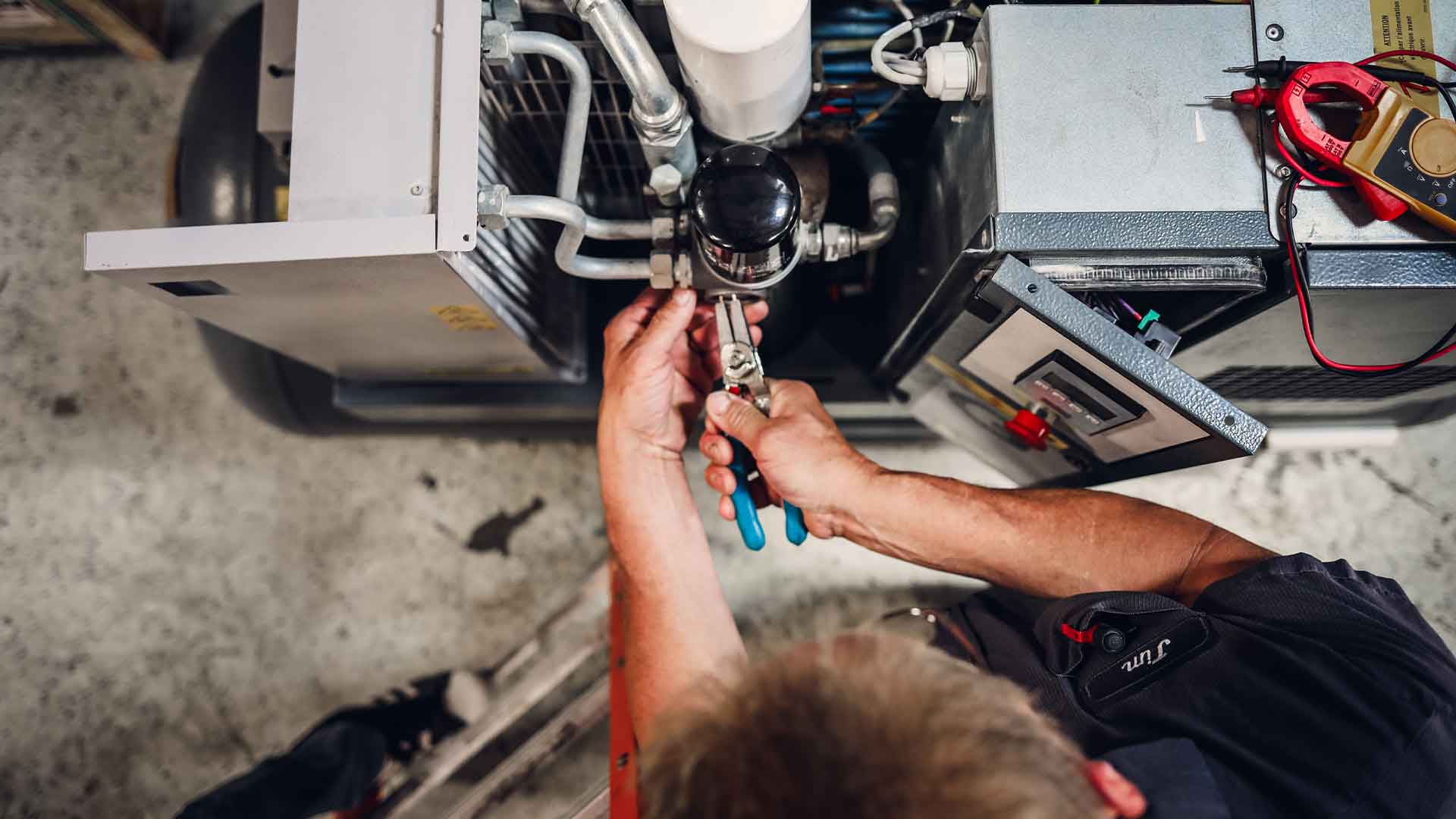 A technician in safety gear meticulously performs maintenance on an air compressor, surrounded by an array of tools and replacement parts, ensuring the machine's optimal performance and reliability.