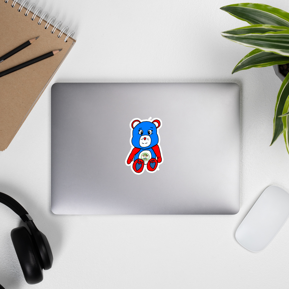 White Desk with a laptop, mouse, a notebook, and supplies. The laptop has a Belizean themed teddy bear sticker on it.