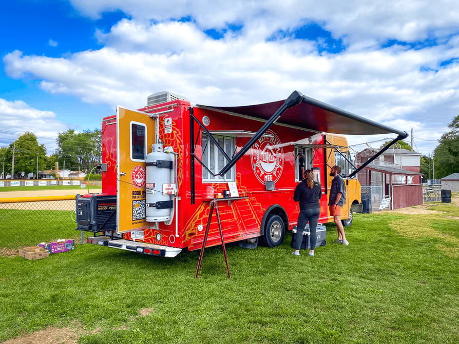 People standing outside food truck parked on grass.