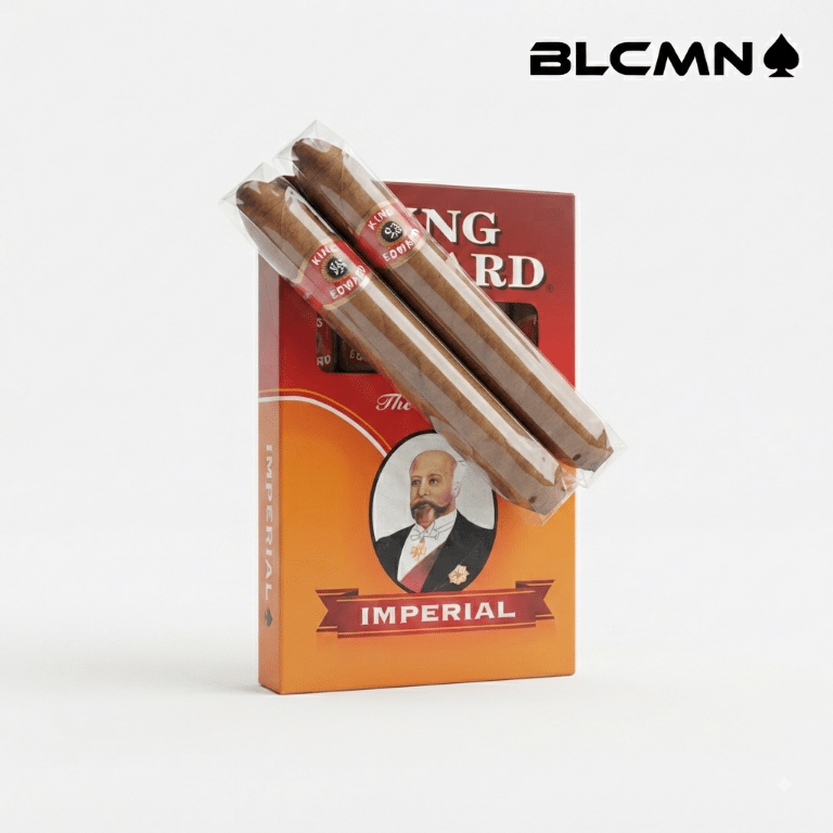 Studio product photograph on a clean white background showing a 5-pack box of King Edward Imperial cigars standing upright, with two individually wrapped cigars placed diagonally across the front of the pack. The black typography logo "BLCMN♠️" is positioned neatly in the top right corner.